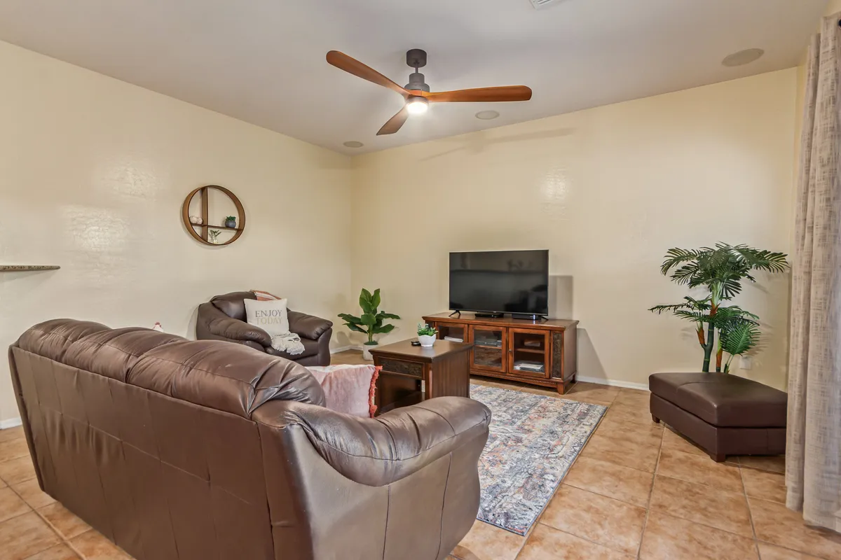 The family room features a comfortable leather sofa, a wooden TV stand, lush greenery from a potted plant, a decorative round mirror, and a soft area rug. The ambiance is cozy and perfect for relaxing, socializing, or enjoying movie nights together.