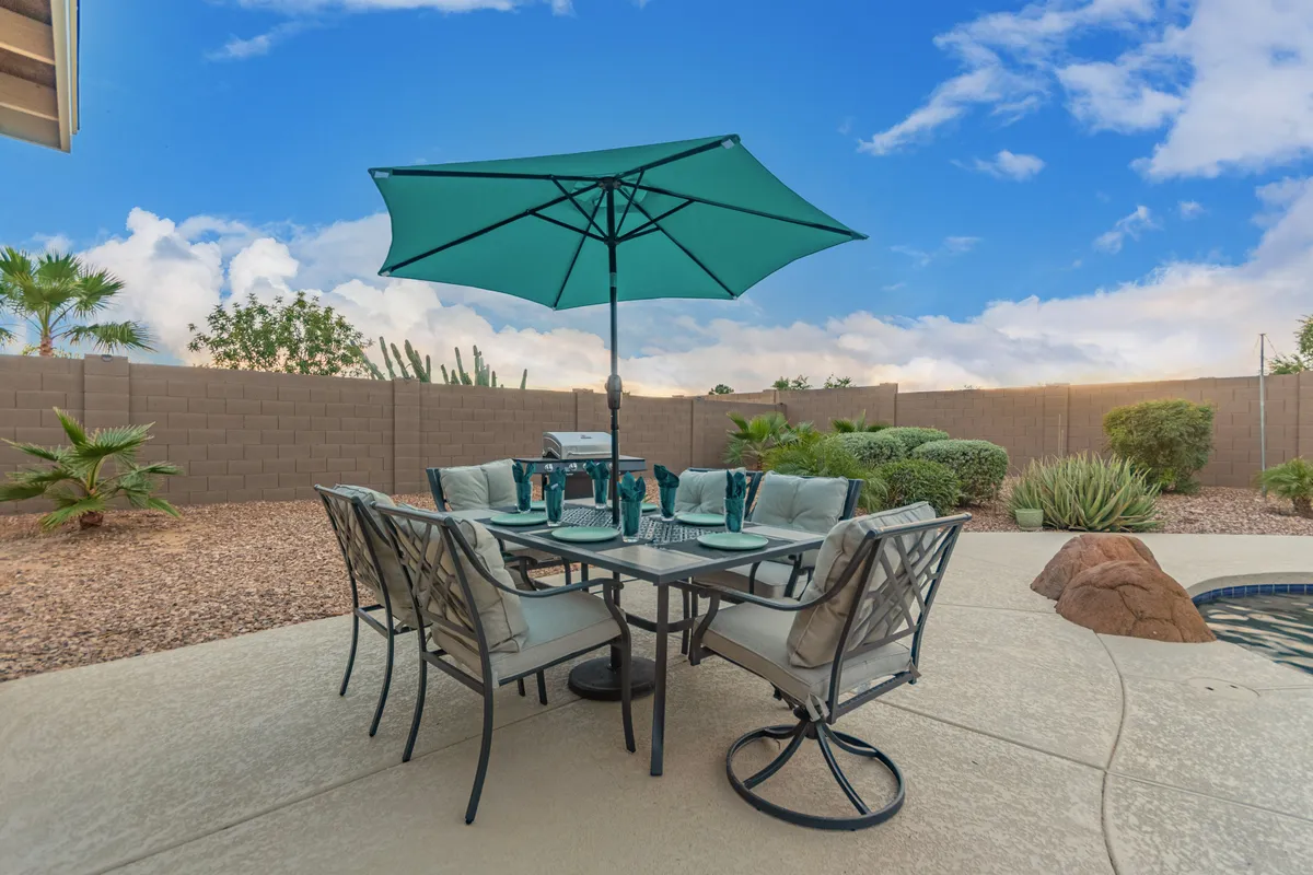 An inviting patio area featuring a dining table shaded by a green umbrella, surrounded by lush plants. The space suggests opportunities for outdoor meals, relaxation, and quality time in the fresh air—activities perfect for dog owners and families.