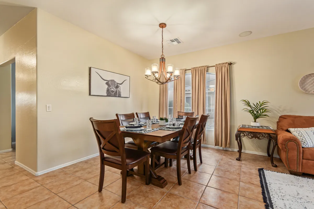 A warm and elegant dining area featuring a table set for eight, illuminated by a chandelier and surrounded by soft curtains and tasteful artwork. The space evokes a sense of intimate gatherings and celebratory dinners.