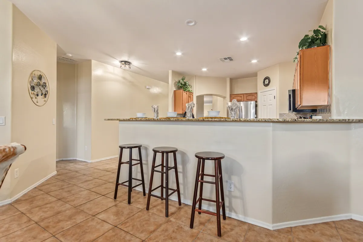 A bright, open kitchen with a spacious island and several bar stools, surrounded by modern cabinetry. The layout is ideal for cooking, entertaining, and casual meals, with clear sightlines that invite gathering and conversation.
