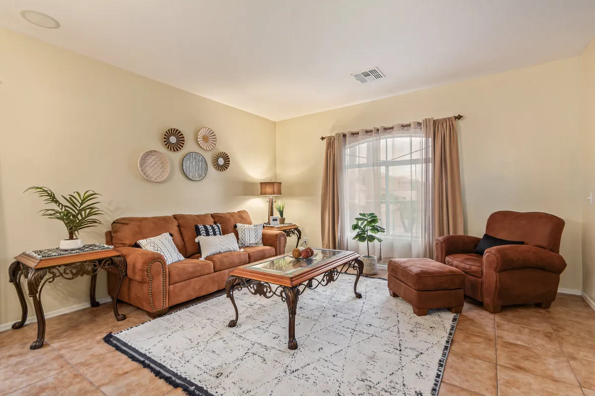 A cozy family room with a brown leather sofa, glass coffee table, decorative wall plates, window with curtains, and a potted plant. The space is arranged for both comfort and socializing, perfect for movie nights or relaxing with loved ones.