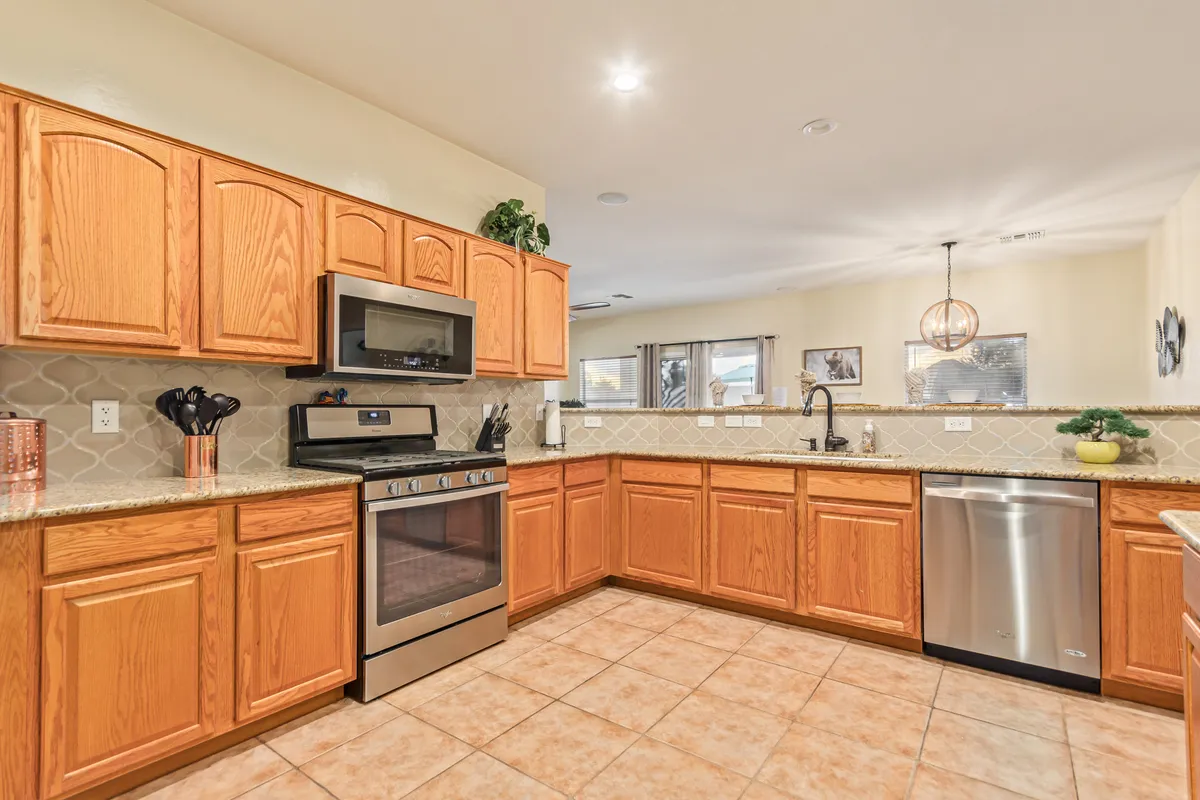 A wide view of the kitchen featuring extensive cabinetry, stainless steel appliances, granite countertops, and a welcoming sink area under soft lighting. The large windows in the background suggest an inviting flow of natural light and views beyond.